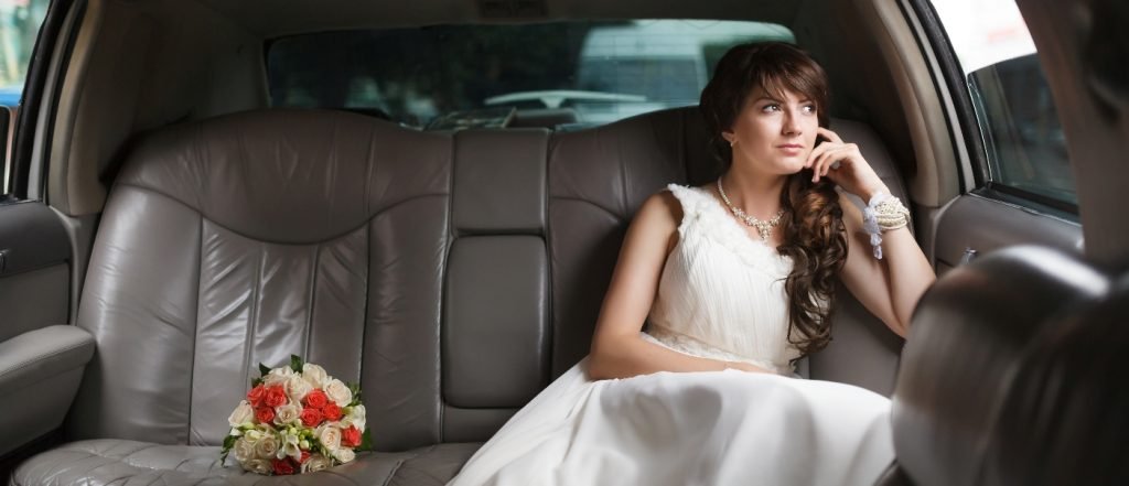 Bride sitting in limousine back seat wearing a white dress and looking from the window