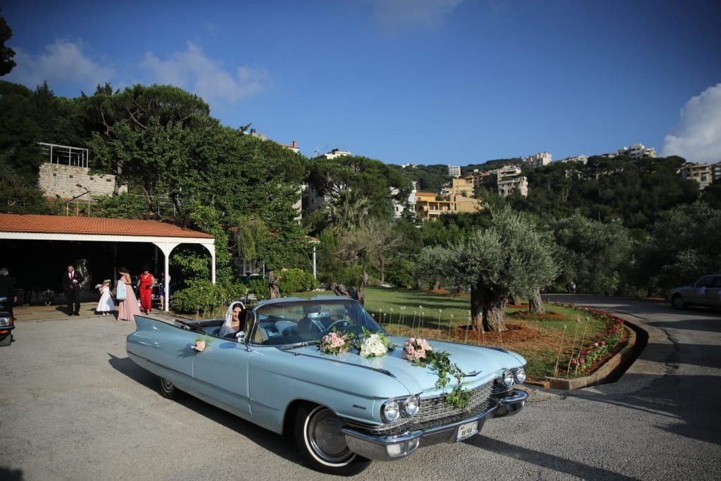 Classic convertible light blue Cadillac 1960 decorated with flowers with the bride sitting inside