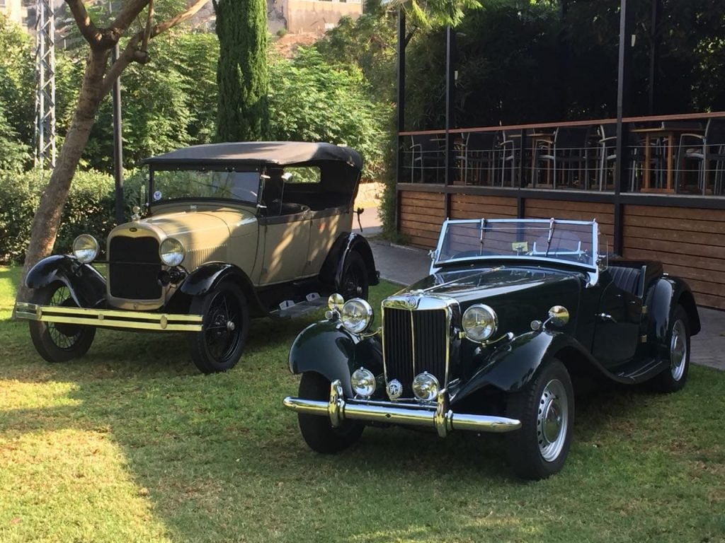 The Ford 1928 parked under a tree next to the MG classic