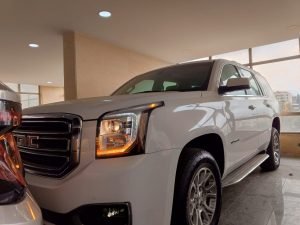 Front of the white GMC 7 seater car with lights on 