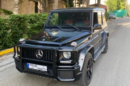 The front of the luxury G class Mercedes black with green trees behind