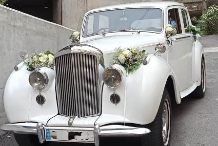 The front of the vintage white Rolls-Royce Bentley wedding car with flower decoration
