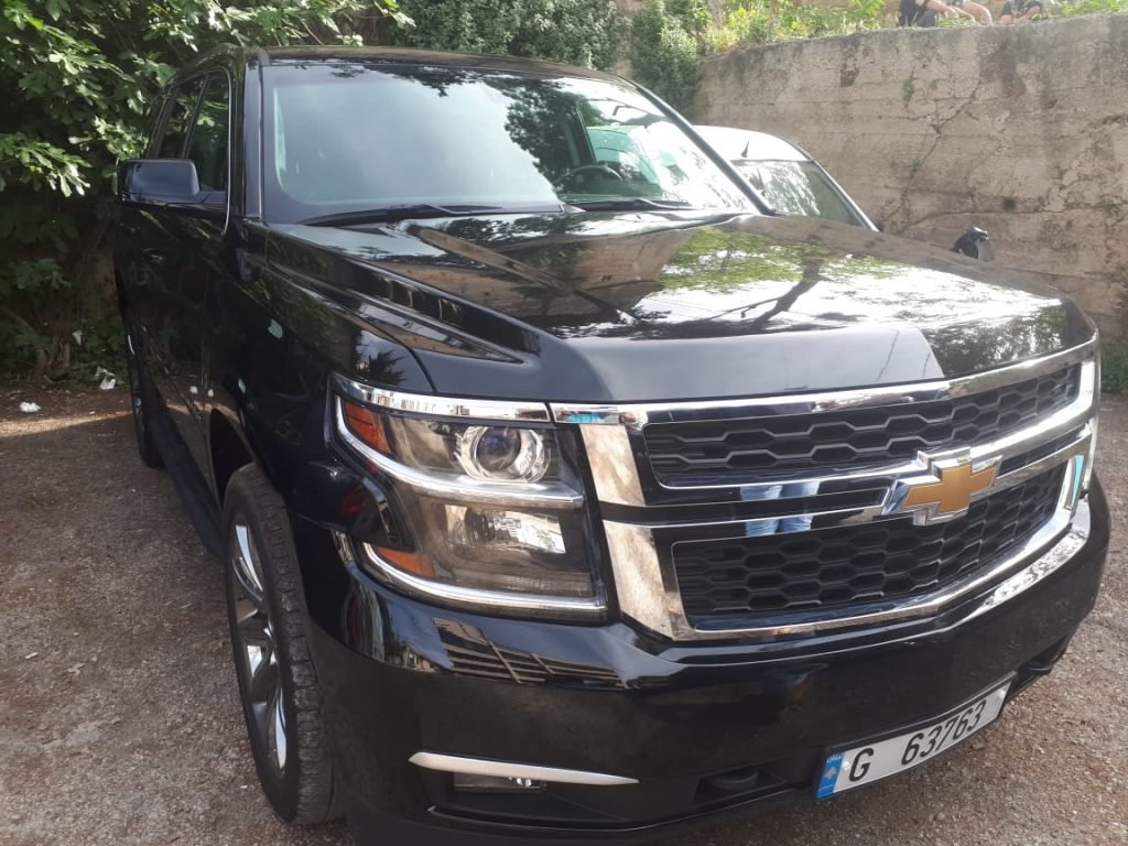 The front side of the luxury Chevrolet Tahoe 2020 black parked in front of a green tree